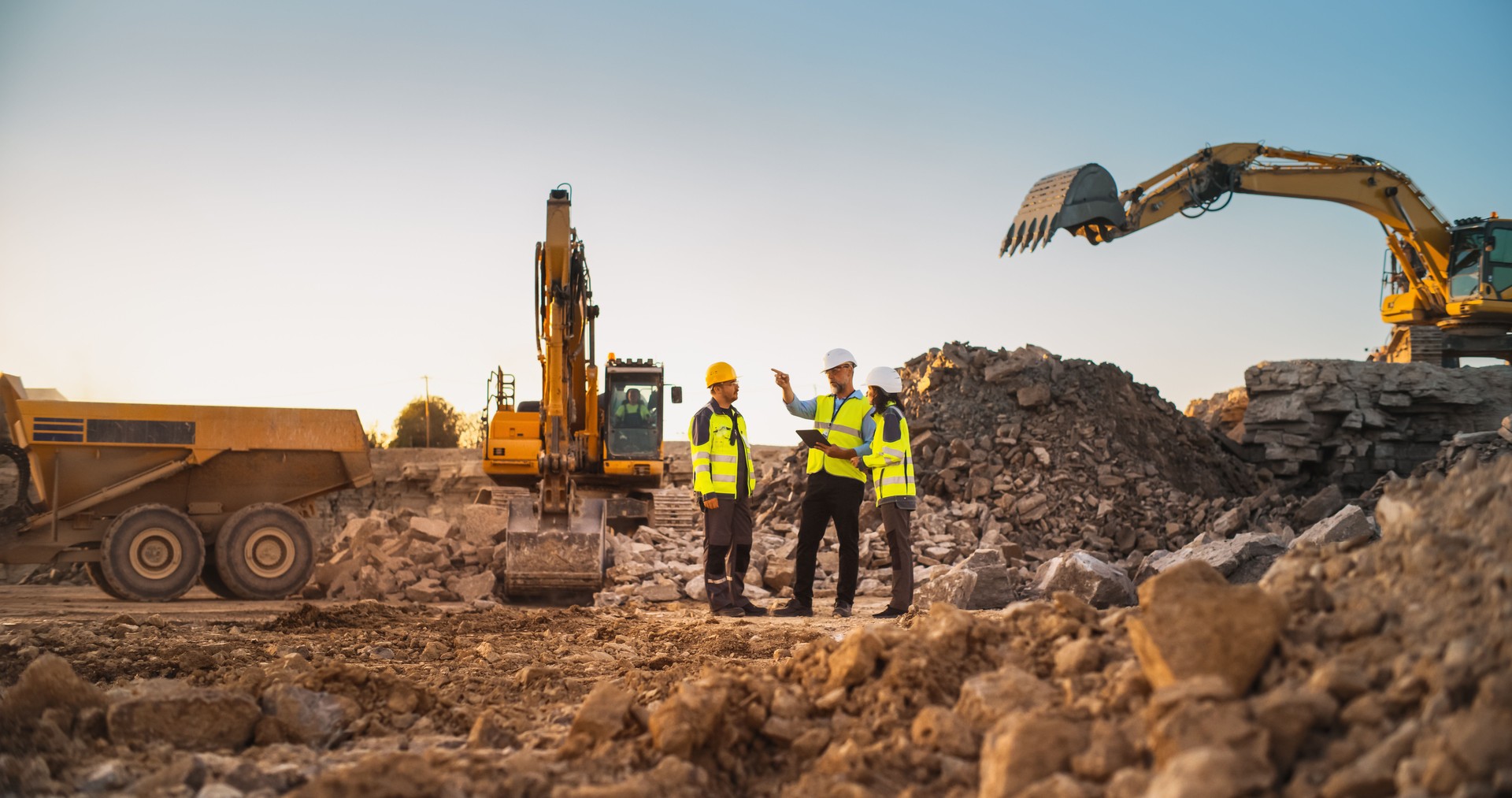 Construction Site With Excavators on Sunny Day: Diverse Team Of Male And Female Real Estate Developers Discussing Project. Engineer, Architect, Investor Talking About Apartment Building, Using Tablet
